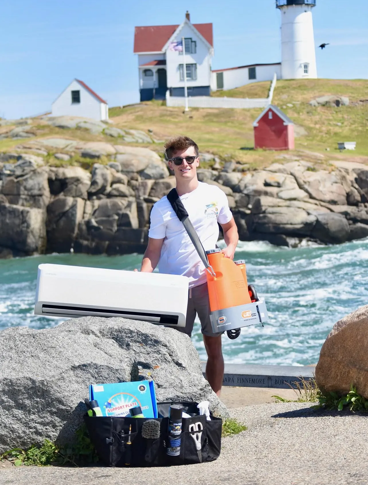 Gavin of Gavin's Mini-Split Cleaning holding a mini-split unit and coil-cleaning equipment at the Nubble Lighthouse in York, Maine